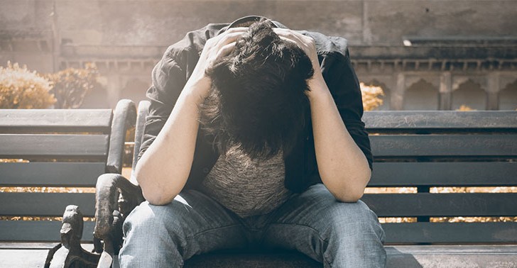 Personne assise sur un banc en extérieur qui se tient la tête dans les mains