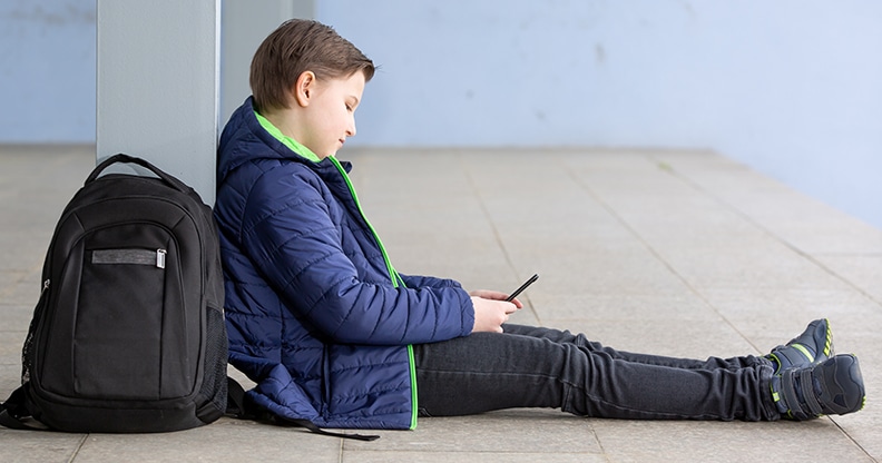 Écolier assis par terre avec son sac à dos et un téléphone cellulaire